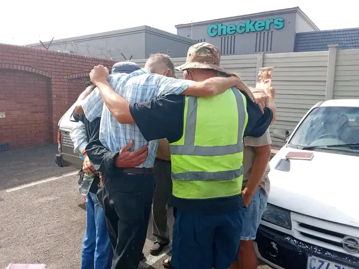 Heart Creations volunteers and local residents standing next to a car, embracing in a warm group hug