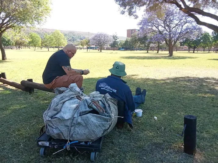 Heart Creations volunteer sitting on the grass in a park, listening and talking quietly with a local resident